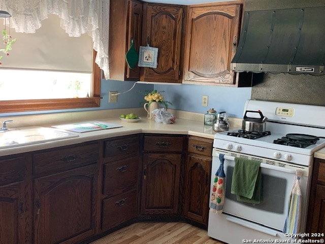 kitchen featuring white gas range oven, light wood-type flooring, dark brown cabinets, sink, and extractor fan