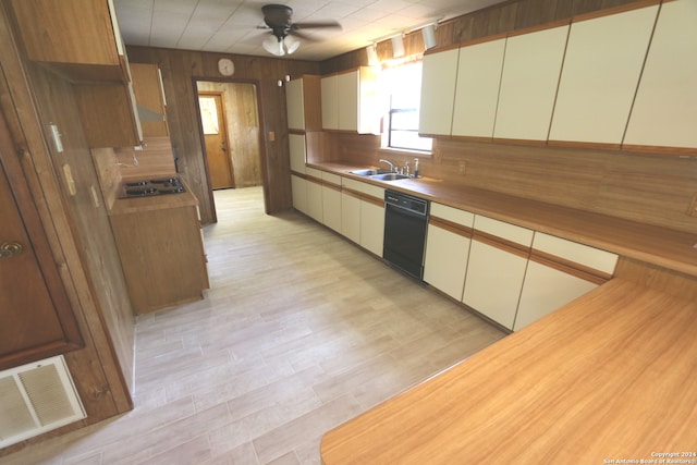 kitchen with black dishwasher, light hardwood / wood-style floors, sink, wood walls, and ceiling fan