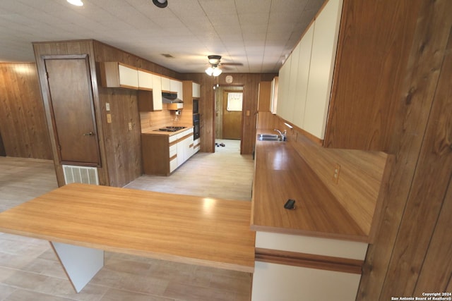 kitchen featuring decorative backsplash, light wood-type flooring, black appliances, ceiling fan, and wooden walls