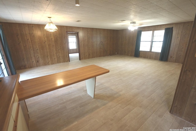 unfurnished dining area with ceiling fan, wood walls, and light hardwood / wood-style floors