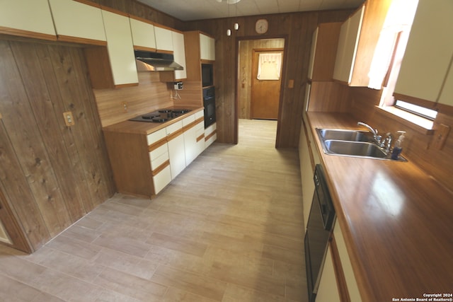 kitchen with white cabinets, wood walls, sink, light hardwood / wood-style flooring, and black appliances