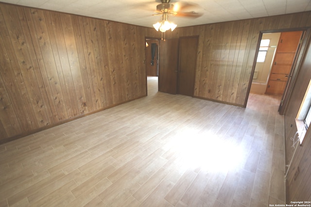 empty room featuring ceiling fan, light hardwood / wood-style flooring, and wood walls