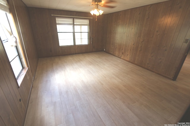 empty room with wood walls, light hardwood / wood-style floors, and ceiling fan