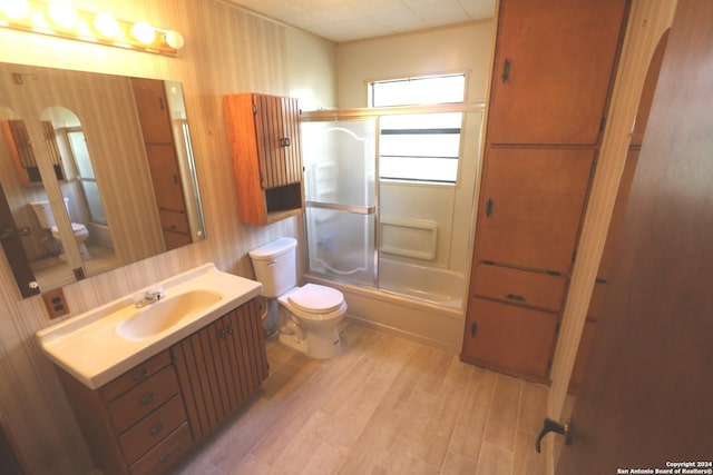 full bathroom with hardwood / wood-style floors, vanity, toilet, and bath / shower combo with glass door