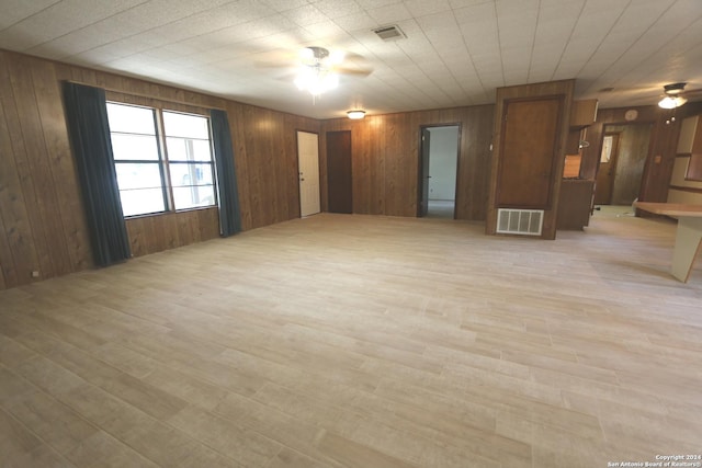 empty room with ceiling fan, light wood-type flooring, and wood walls