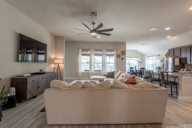 living room featuring ceiling fan, a textured ceiling, light wood-type flooring, and vaulted ceiling