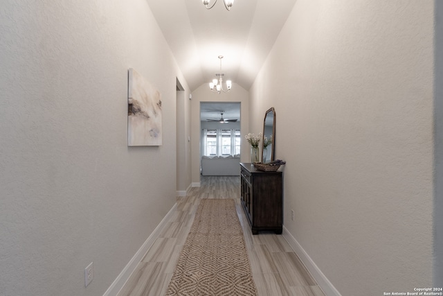 hallway with light hardwood / wood-style floors, lofted ceiling, and a notable chandelier