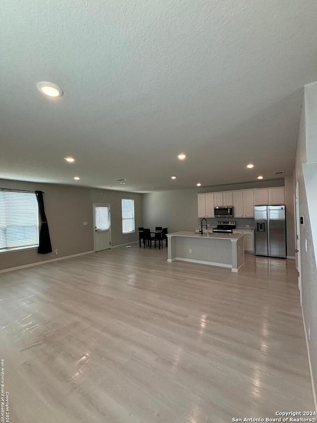 unfurnished living room with a textured ceiling, light hardwood / wood-style floors, and sink