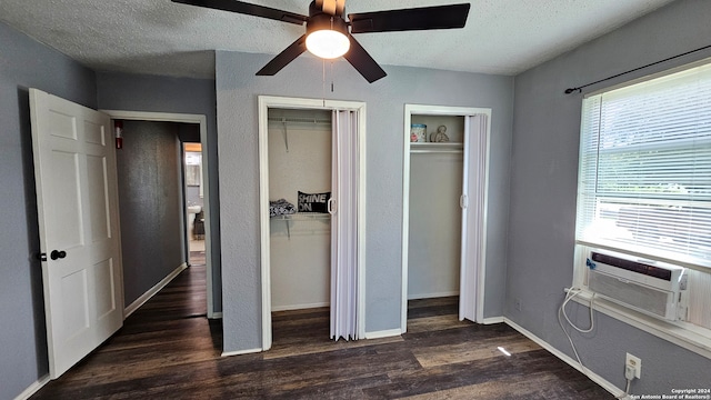 unfurnished bedroom with a textured ceiling, cooling unit, multiple closets, dark hardwood / wood-style flooring, and ceiling fan