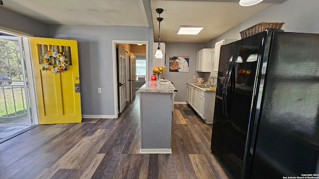 kitchen featuring dark hardwood / wood-style floors, black fridge, sink, white cabinets, and hanging light fixtures