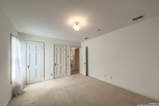 unfurnished bedroom with light colored carpet and two closets