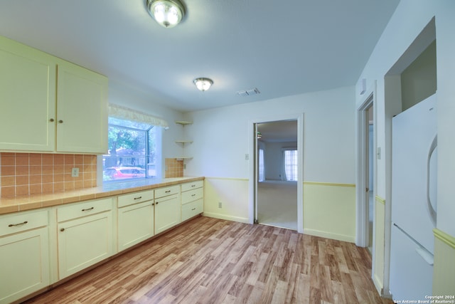 kitchen featuring light wood-type flooring, backsplash, tile countertops, and white refrigerator