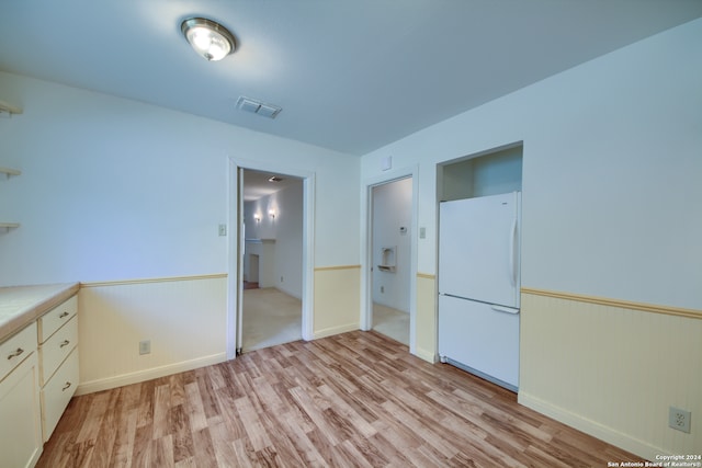 interior space with light hardwood / wood-style flooring, white refrigerator, and cream cabinetry