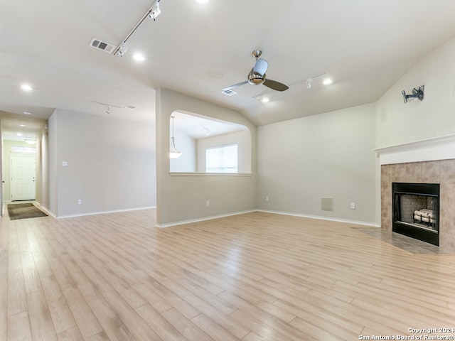 unfurnished living room featuring ceiling fan, lofted ceiling, track lighting, a tile fireplace, and light wood-type flooring