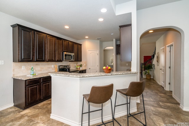 kitchen with light stone counters, dark brown cabinetry, black electric range oven, kitchen peninsula, and backsplash