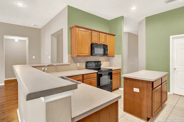 kitchen featuring light tile patterned floors, kitchen peninsula, backsplash, black appliances, and a center island