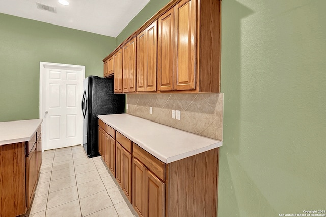 kitchen with backsplash, light tile patterned floors, and black refrigerator