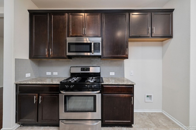 kitchen featuring baseboards, appliances with stainless steel finishes, light stone counters, dark brown cabinets, and backsplash