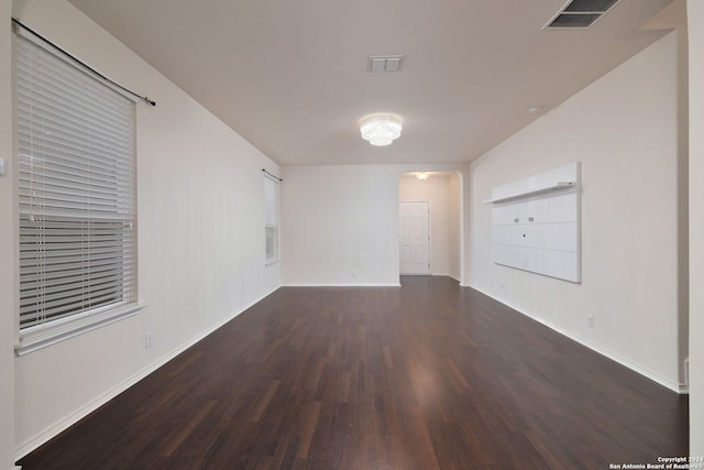 spare room featuring arched walkways, dark wood-style flooring, visible vents, and baseboards