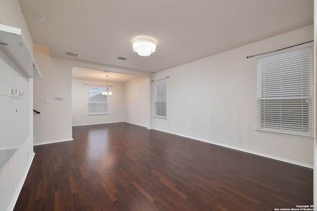 empty room featuring baseboards, dark wood-style flooring, visible vents, and a notable chandelier