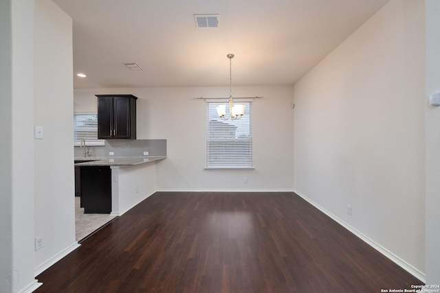 unfurnished dining area featuring baseboards, visible vents, dark wood-style floors, a chandelier, and a sink