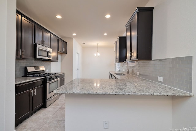 kitchen with light stone counters, a peninsula, stainless steel appliances, pendant lighting, and a sink