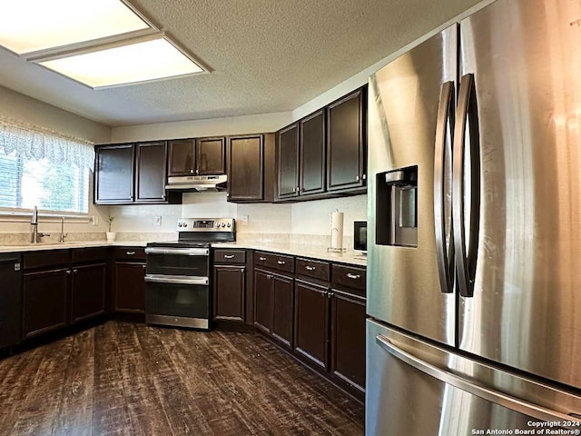 kitchen with a textured ceiling, dark wood-type flooring, sink, appliances with stainless steel finishes, and dark brown cabinetry