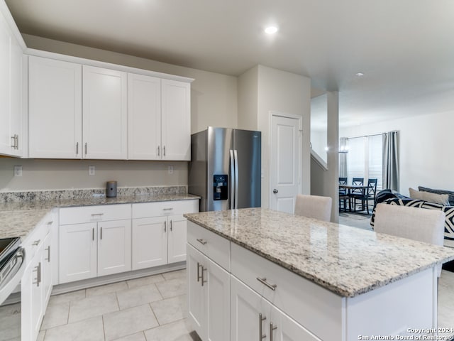 kitchen featuring light stone countertops, a kitchen island, stainless steel appliances, and white cabinetry