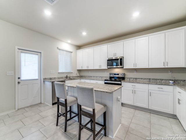 kitchen featuring light stone counters, white cabinets, a kitchen island, stainless steel appliances, and a breakfast bar