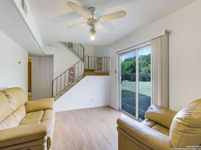 living room featuring light hardwood / wood-style floors, ceiling fan, and a textured ceiling