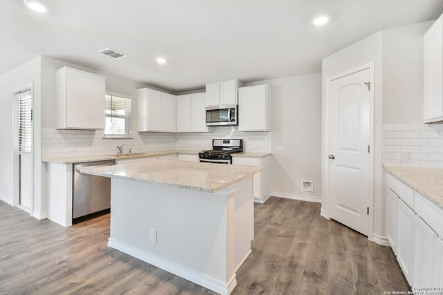 kitchen with white cabinets, a kitchen island, appliances with stainless steel finishes, light stone countertops, and light hardwood / wood-style floors