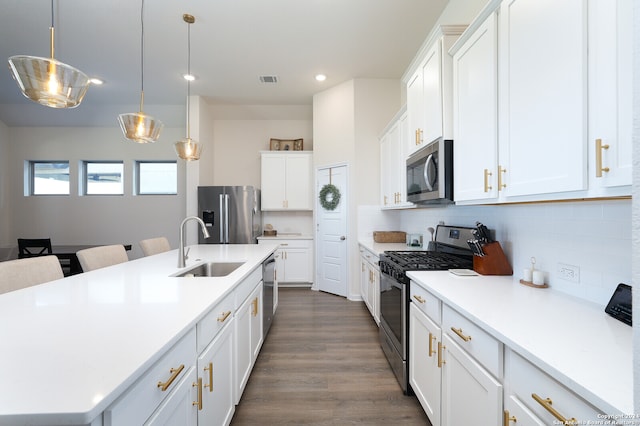 kitchen with white cabinets, dark hardwood / wood-style flooring, pendant lighting, stainless steel appliances, and a center island with sink