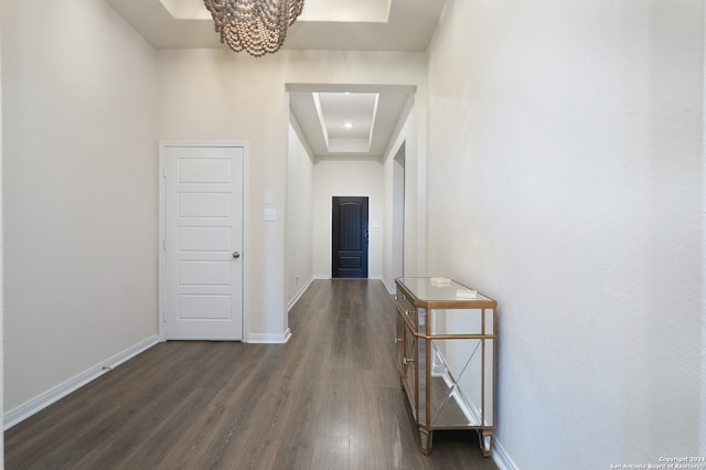 corridor with a tray ceiling, dark hardwood / wood-style floors, and a chandelier