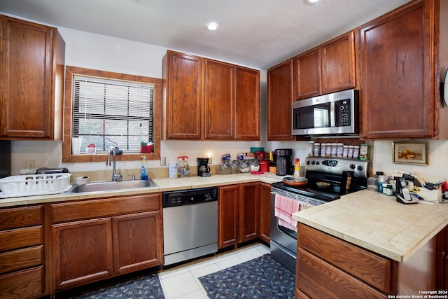 kitchen with appliances with stainless steel finishes, a textured ceiling, sink, and light tile patterned floors