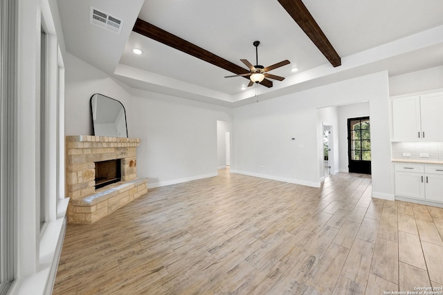 unfurnished living room featuring light hardwood / wood-style floors, a fireplace, beam ceiling, and ceiling fan