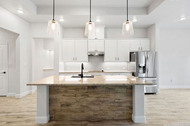 kitchen with light stone countertops, white cabinets, a kitchen island with sink, and stainless steel fridge