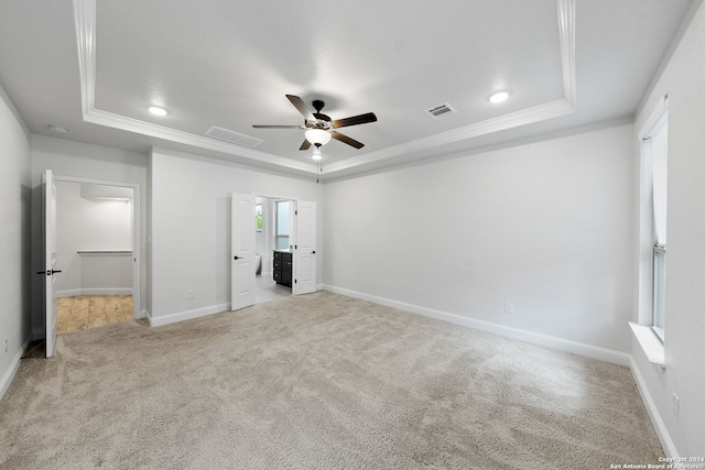 unfurnished bedroom with ornamental molding, a tray ceiling, light carpet, and ceiling fan