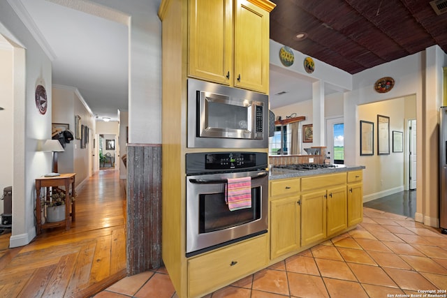 kitchen with light brown cabinets, appliances with stainless steel finishes, ornamental molding, and light hardwood / wood-style flooring