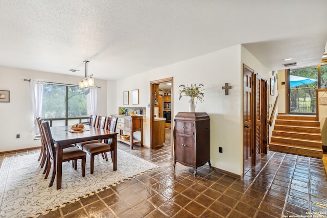 dining room featuring an inviting chandelier, dark tile patterned flooring, and a textured ceiling