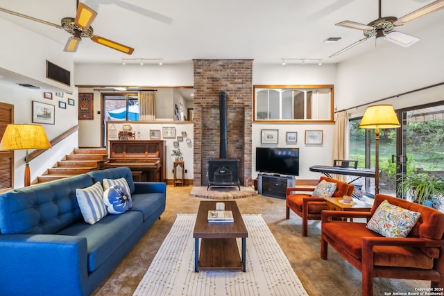 carpeted living room with a wood stove, ceiling fan, and rail lighting