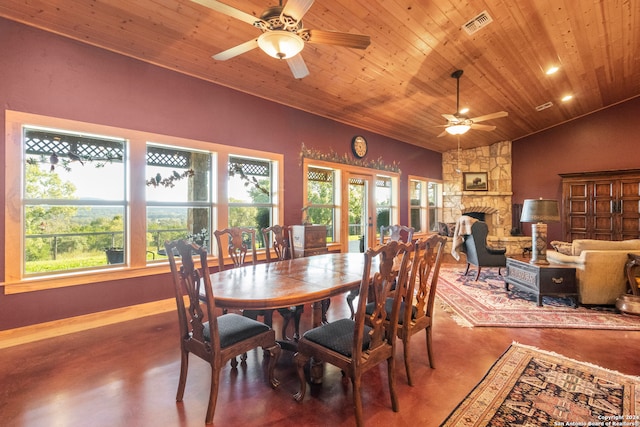 dining space featuring wood ceiling, vaulted ceiling, a stone fireplace, ceiling fan, and concrete flooring