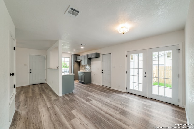 unfurnished living room featuring light wood-type flooring, a textured ceiling, and french doors