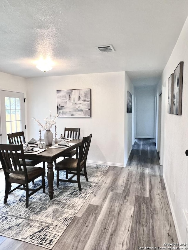 dining area with wood finished floors, a textured ceiling, baseboards, and visible vents