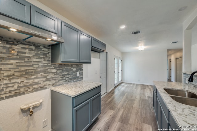 kitchen featuring backsplash, sink, hardwood / wood-style flooring, light stone countertops, and extractor fan