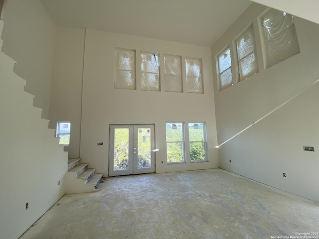unfurnished living room featuring stairway, french doors, and a towering ceiling
