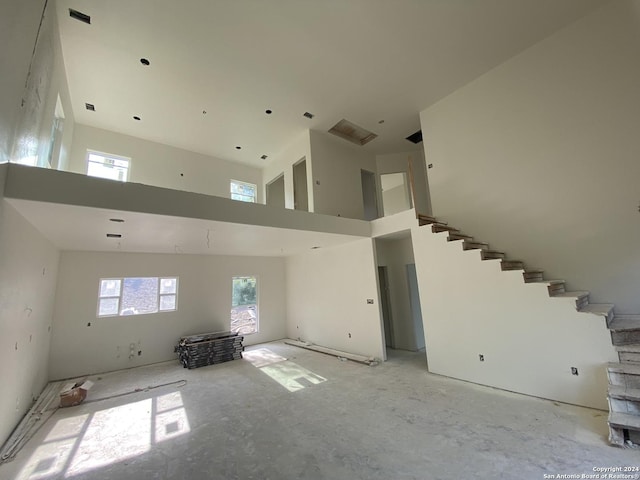 unfurnished living room featuring stairway and a towering ceiling