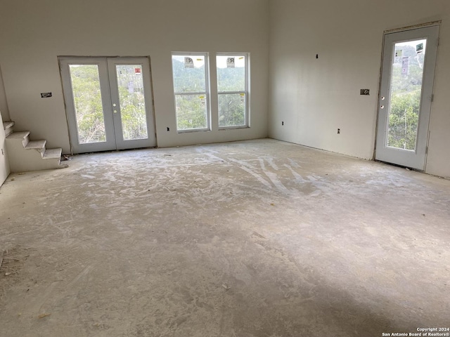 unfurnished living room featuring french doors, stairs, and concrete flooring