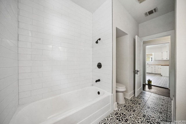 bathroom featuring tiled shower / bath combo, toilet, and tile patterned floors