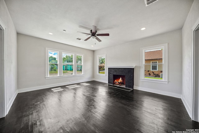 unfurnished living room with a fireplace, dark wood-type flooring, ceiling fan, and plenty of natural light