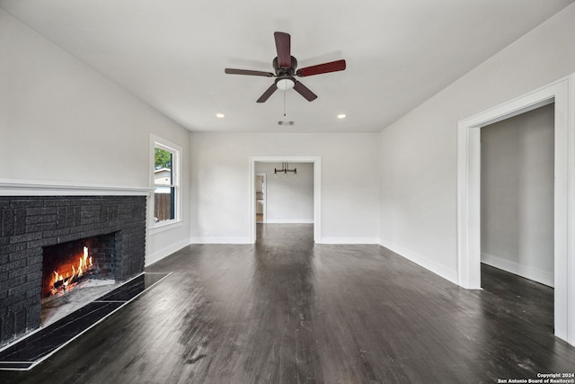 unfurnished living room featuring dark hardwood / wood-style flooring, ceiling fan, and a brick fireplace